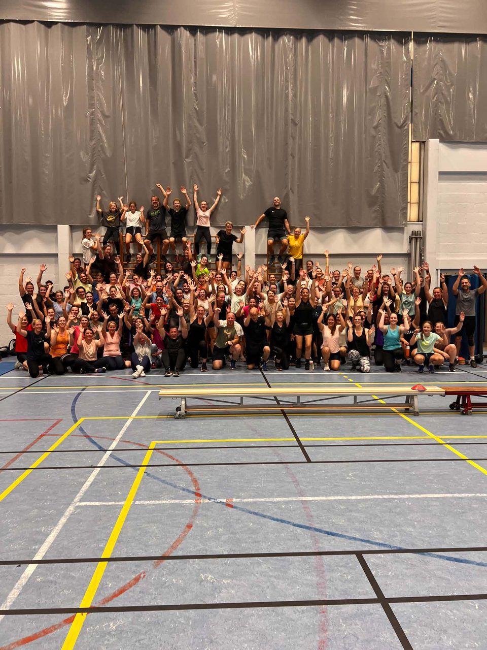 Deelnemers van de bootcamp groepsles van Activate Performance juichen met de armen omhoog in de sporthal in Balen